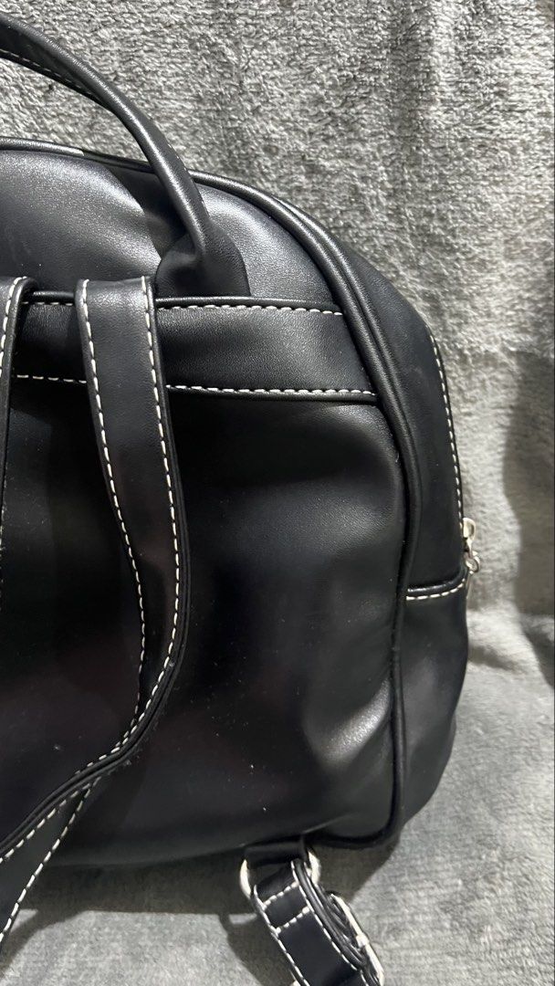 Black leather mini backpack (Category: Backpacks) located in Manila. Submitted by asdfghjkl.mountain (Listing ID 1470278269, Image 3). Description: - Color & Material: Black faux leather - Design: White contrast stitching along seams and straps - Storage: Front zipped pocket with round silver puller - Carry Options: Adjustable shoulder straps and top carry handle - Size: Small everyday mini backpack.
