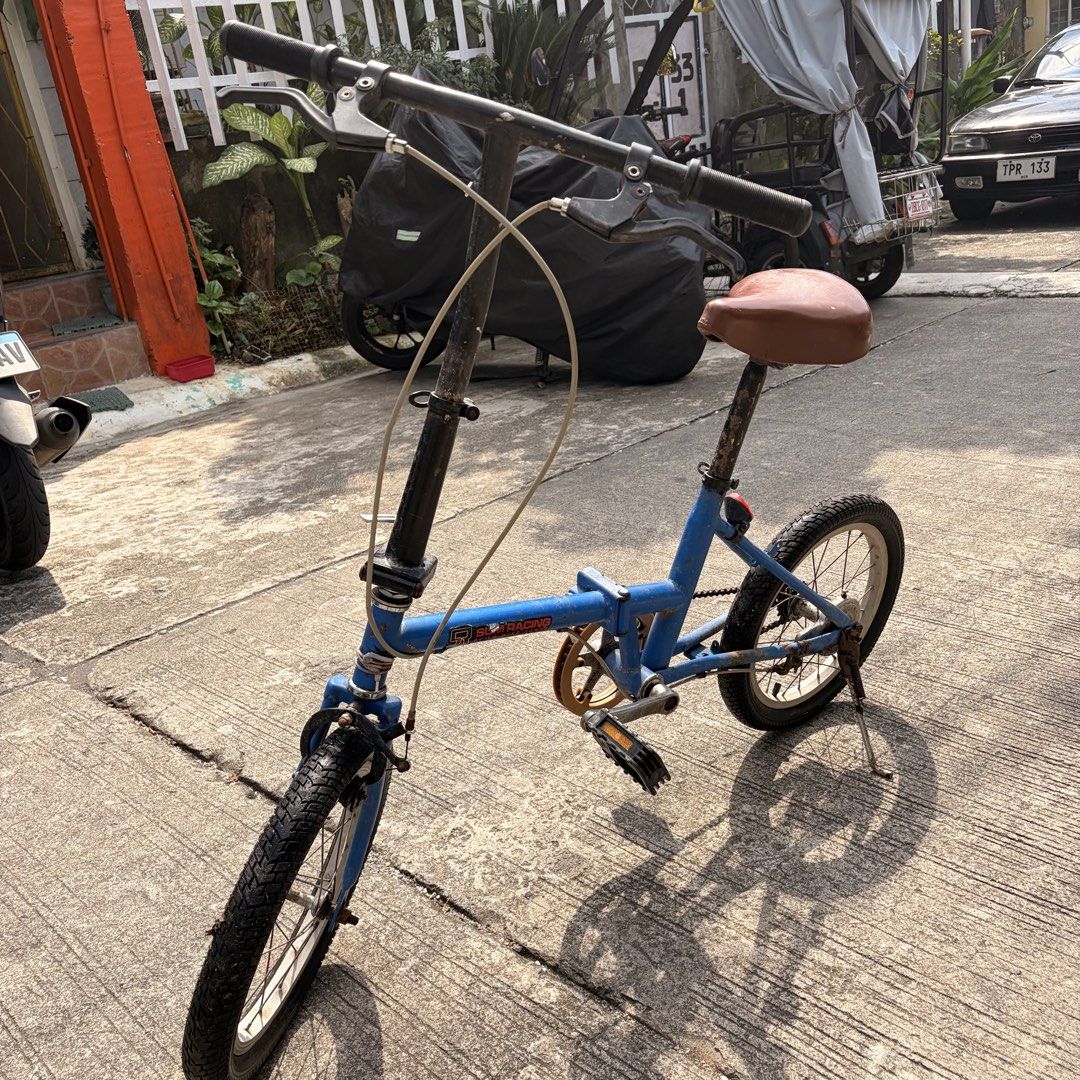 Blue Japanese Folding Bike (Category: Bicycles) located in Manila. Submitted by happy.lorryy (Listing ID 1470204817, Image 1). Description: - Brand/Model: Blue Japanese folding bike - Design: Compact and easily foldable for transport or small storage spaces - Features: Standard handlebars, brown saddle, and kickstand attached - Condition: Significant rust, wear, and peeling paint throughout (tires, chain, and frame) - Note: Needs restoration or p