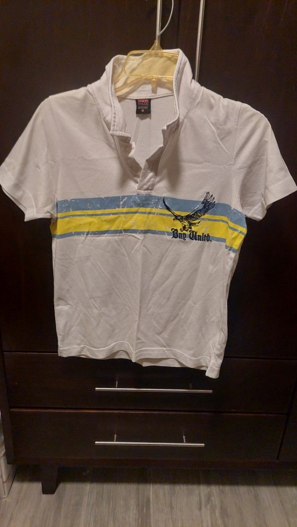 Bny Unltd White Polo Shirt with Graphic Eagle Print (Category: Tshirts & Polo Shirts ) located in Paranaque City. Submitted by daddyu (Listing ID 1470179111, Image 2). Description: - Brand: BNY Unltd. - Color: White with bold blue and yellow chest stripes - Design: Flying eagle graphic with BNY Unltd. lettering - Details: Short sleeves, classic collar, front button-down closure - Condition/Fit: Casual everyday wear, size tag visible on inner coll