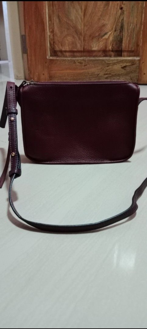 Burgundy Leather Crossbody Bag (Category: Cross-body Bags) located in Mangaldan. Submitted by closetqwin (Listing ID 1470216503, Image 2). Description: - First photo inspo only - Material: Premium dark burgundy pebbled leather with gold-tone hardware - Design: Clean silhouette with a structured base and subtle branding - Closure: Secure top zip closure - Storage: Exterior zippered back pocket with leather pull tabs - Strap: Adjustable strap for c