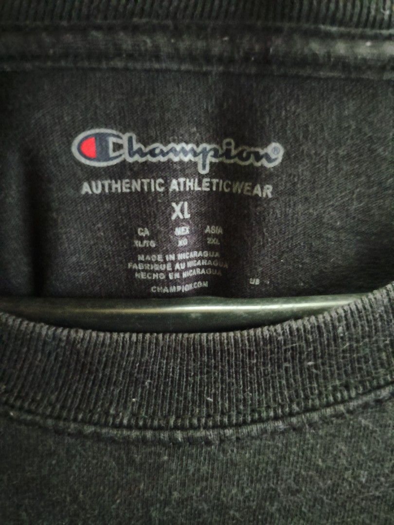 Champion Black T-Shirt (Category: Tshirts & Polo Shirts ) located in Buug. Submitted by zigeldz_a1721a (Listing ID 1470299901, Image 3). Description: - Brand: Champion - Color: Charcoal Black - Fit: Regular fit - Neckline: Classic crew neck - Sleeves: Short sleeves with signature embroidered logo patch on the left cuff - Style: Casual, athletic wear - Condition: Excellent / Pre-loved (ready to wear) - Pair it with: Jeans, shorts, or joggers for a