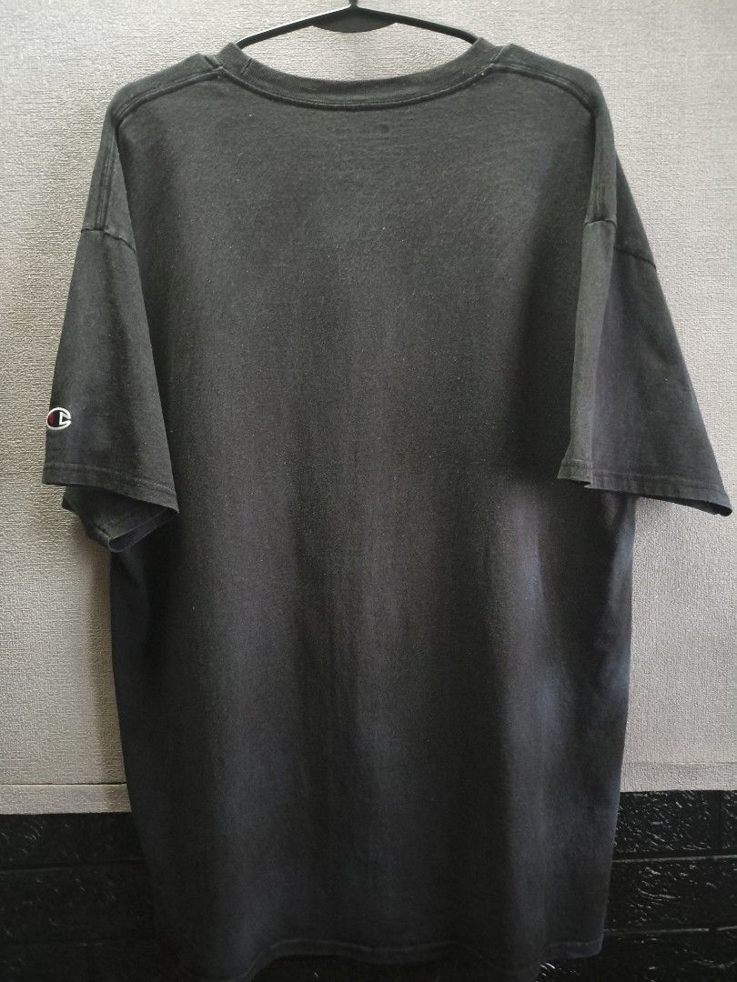 Champion Black T-Shirt (Category: Tshirts & Polo Shirts ) located in Buug. Submitted by zigeldz_a1721a (Listing ID 1470299901, Image 2). Description: - Brand: Champion - Color: Charcoal Black - Fit: Regular fit - Neckline: Classic crew neck - Sleeves: Short sleeves with signature embroidered logo patch on the left cuff - Style: Casual, athletic wear - Condition: Excellent / Pre-loved (ready to wear) - Pair it with: Jeans, shorts, or joggers for a