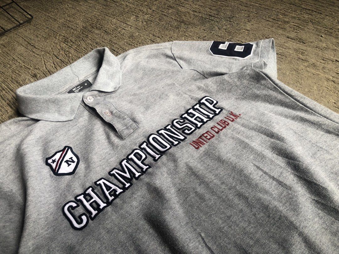 Championship polo men’s (Category: Tshirts & Polo Shirts ) located in Zamboanga. Submitted by wayne_geroche16 (Listing ID 1470309864, Image 3). Description: - Brand: NET men - Color: Grey - Size: Medium (Tagged M) -width: 19.5 -length: 25.5 - Design: Bold Championship United Club U.K. embroidery across the chest - Details: Shield logo patch on right chest, number 6 patch on left sleeve - Features: Classic collar with a three-button placket - Cond