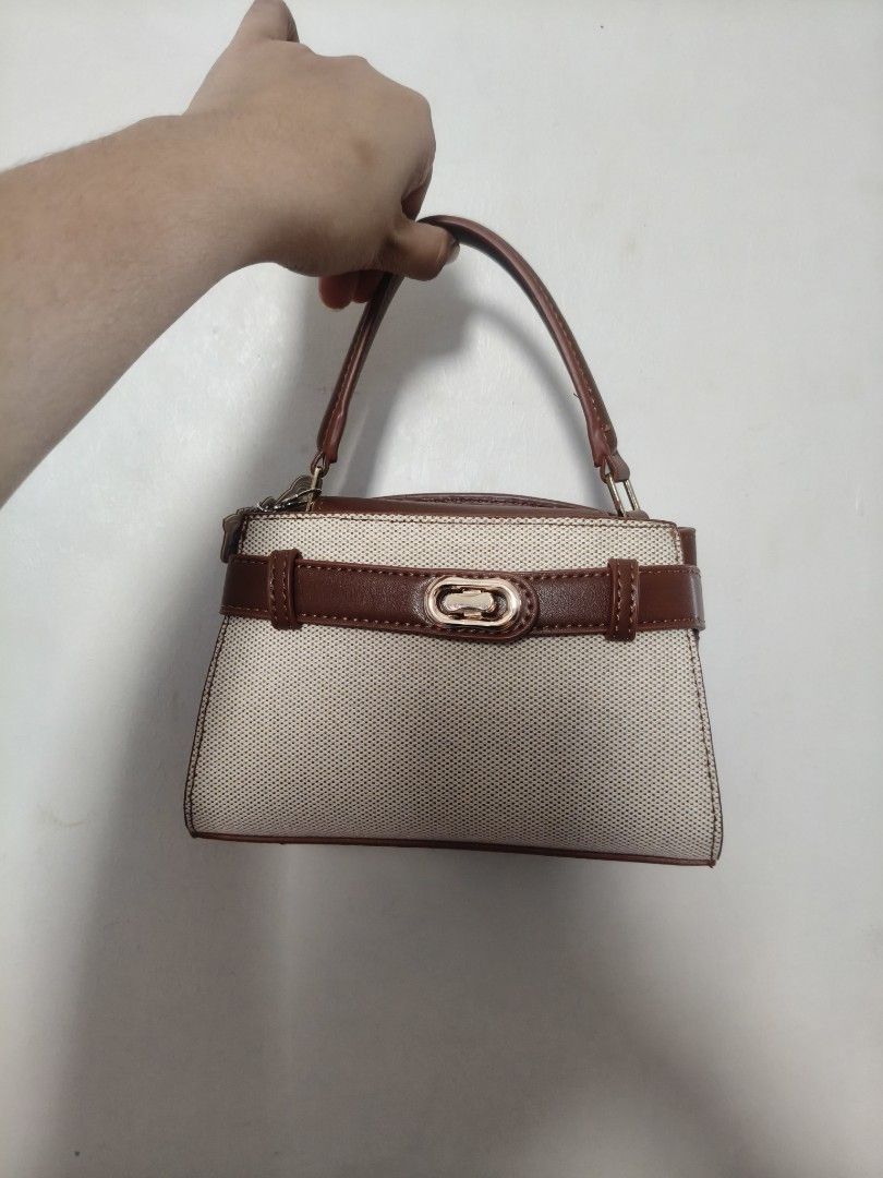 Charles & Keith Brown and Beige Canvas Handbag (Category: Luxury Bags & Wallets) located in San Fernando. Submitted by pollygirl08 (Listing ID 1470172872, Image 1). Description: - Brand: Charles & Keith - Material: Brown and beige canvas with leather details - Hardware: Gold-tone throughout with clear exterior brand embossing - Design: Structured shape with a top handle and decorative front buckle - Strap: Includes adjustable strap (still in prot