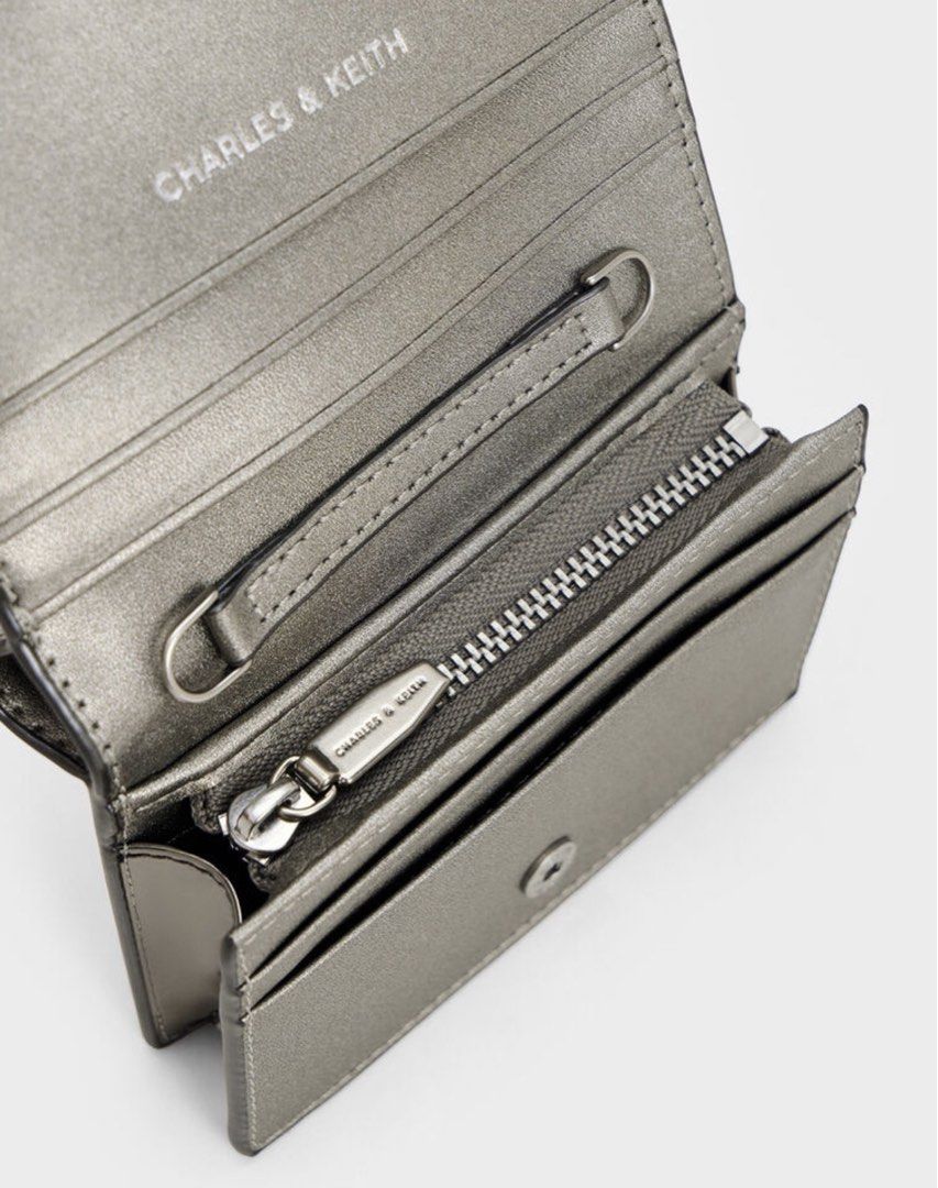 Charles & Keith Metallic Silver Crossbody Bag Wallet (Category: Wallets & Card holders) located in Manila. Submitted by manilynpitero (Listing ID 1470143755, Image 3). Description: - Brand: Charles & Keith - Color: Metallic silver with silver-tone hardware - Design: Double buckle strap detail on the front - Strap: Includes a chain strap for shoulder or crossbody wear - Interior: Features card slots, a zippered coin compartment, and structured poc