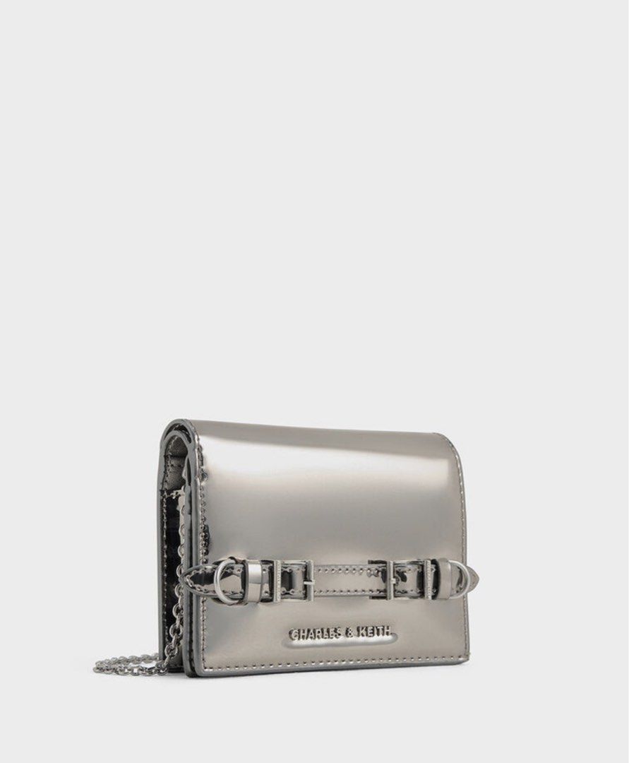 Charles & Keith Metallic Silver Crossbody Bag Wallet (Category: Wallets & Card holders) located in Manila. Submitted by manilynpitero (Listing ID 1470143755, Image 2). Description: - Brand: Charles & Keith - Color: Metallic silver with silver-tone hardware - Design: Double buckle strap detail on the front - Strap: Includes a chain strap for shoulder or crossbody wear - Interior: Features card slots, a zippered coin compartment, and structured poc