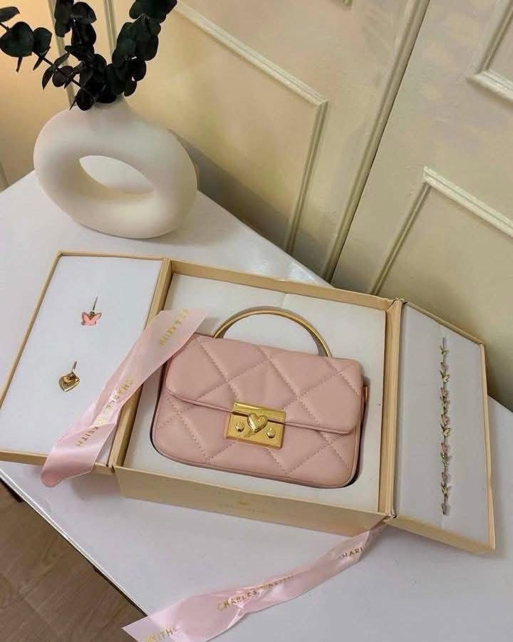 Charles & Keith Quilted Pink Handle Bag Gift Set (Category: Cross-body Bags) located in Manila. Submitted by manilynpitero (Listing ID 1470143470, Image 1). Description: - Brand: Charles & Keith - Style: Pink quilted shoulder bag with gold hardware, top handle, chain strap, and heart clasp closure - Inclusions: Matching butterfly and flower charms, plus an earrings and bracelet set - Packaging: Comes in an original presentation box with ribbon .