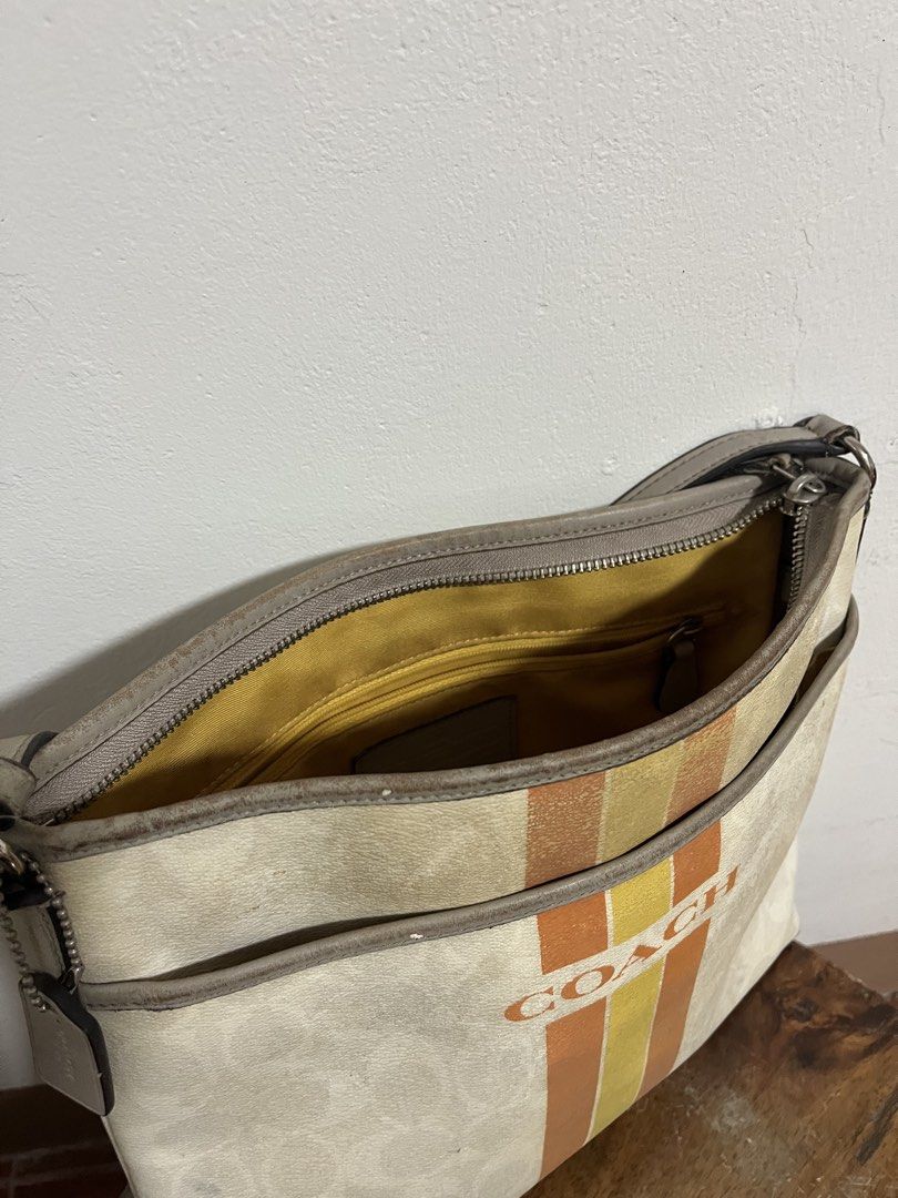 Coach Varsity Stripe Messenger Crossbody Bag (Category: Luxury Bags & Wallets) located in Cabuyao City. Submitted by rdtrmt (Listing ID 1470198165, Image 3). Description: - Brand: Coach - Style: Crossbody bag - Color/Design: Off-white signature C monogram with vertical orange and yellow center stripes - Trim & Hardware: Gray trim with silver-tone hardware - Interior: Bright yellow fabric lining with a convenient interior zip pocket - Exterior: Fr