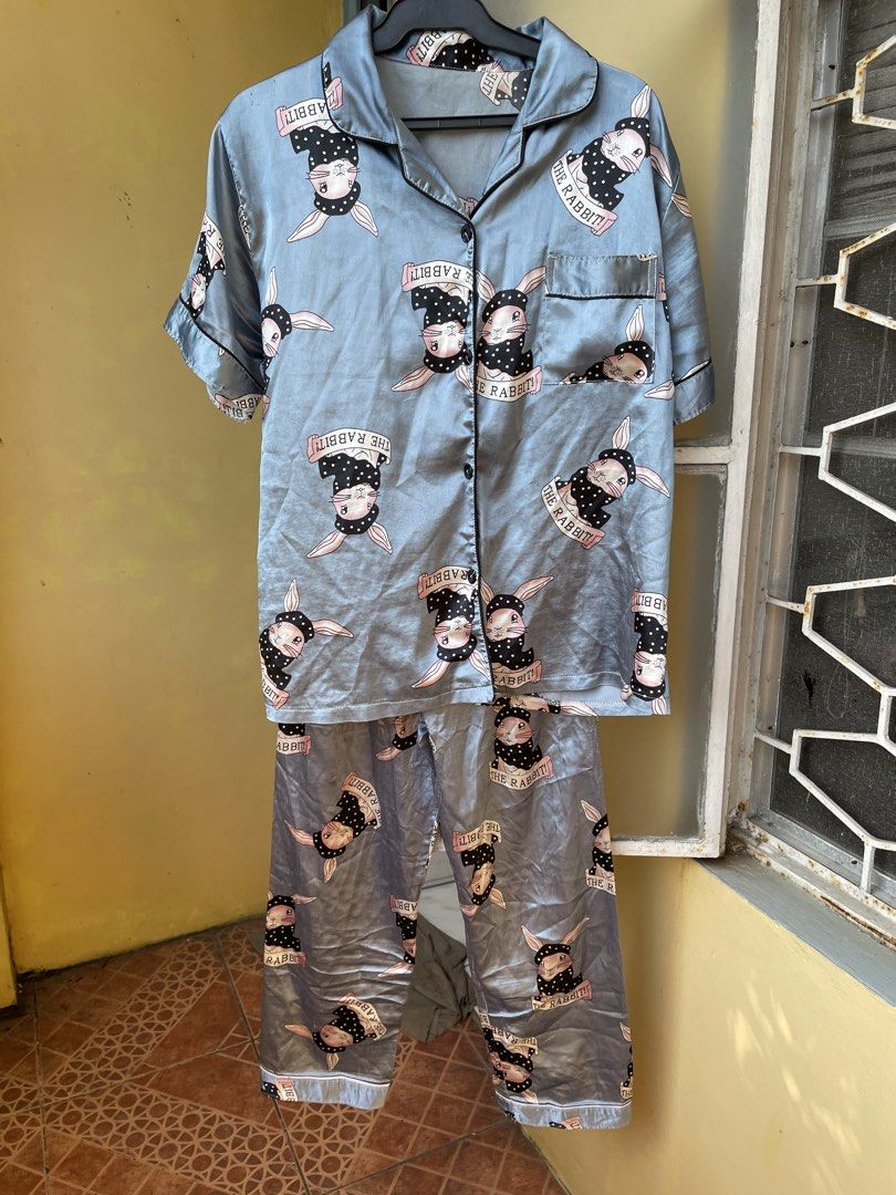 Cute Rabbit Print Satin Pajama Set (Category: Undergarments & Loungewear) located in Pasig City. Submitted by khaleisi (Listing ID 1470227972, Image 1). Description: - Color: Stylish greyish-blue with all-over 'THE RABBIT!' cartoon graphic print - Set includes: Short-sleeve button-up top and matching long pants - Features: Convenient left chest pocket and chic black polka dot headscarf bunny design - Material: Soft, silky, and lightweight satin f