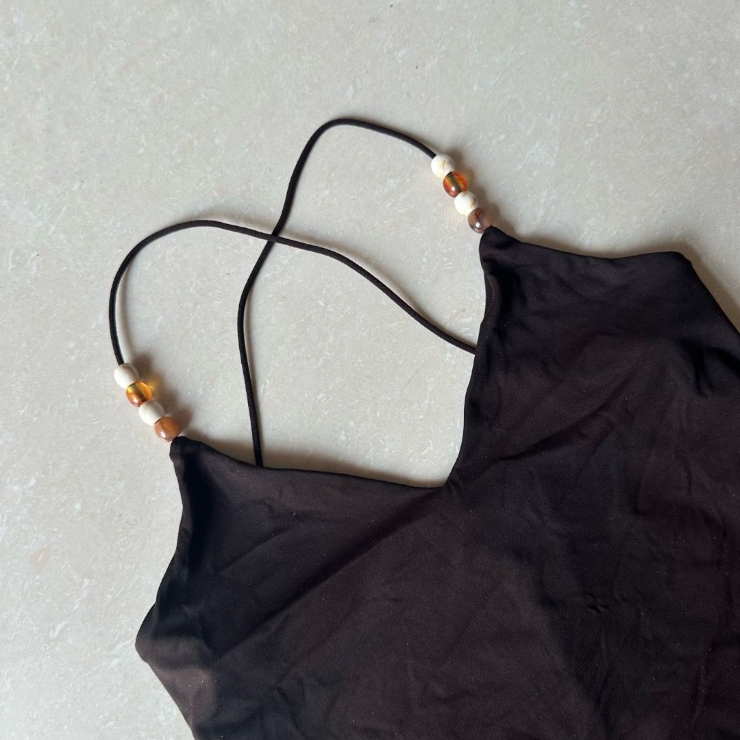 Dark Brown Tank Top with Beaded Straps (Category: Sleeveless) located in Paranaque City. Submitted by yanie.ae (Listing ID 1470165846, Image 2). Description: - Color: Dark brown - Material: Soft, stretchy jersey fabric - Design: Deep V-neckline (front and back) with sleeveless cut - Details: Thin crisscross straps accented with wooden and amber-colored beads - Fit: Form-fitting and hugs the body nicely - Versatility: Great for warm weather or lay