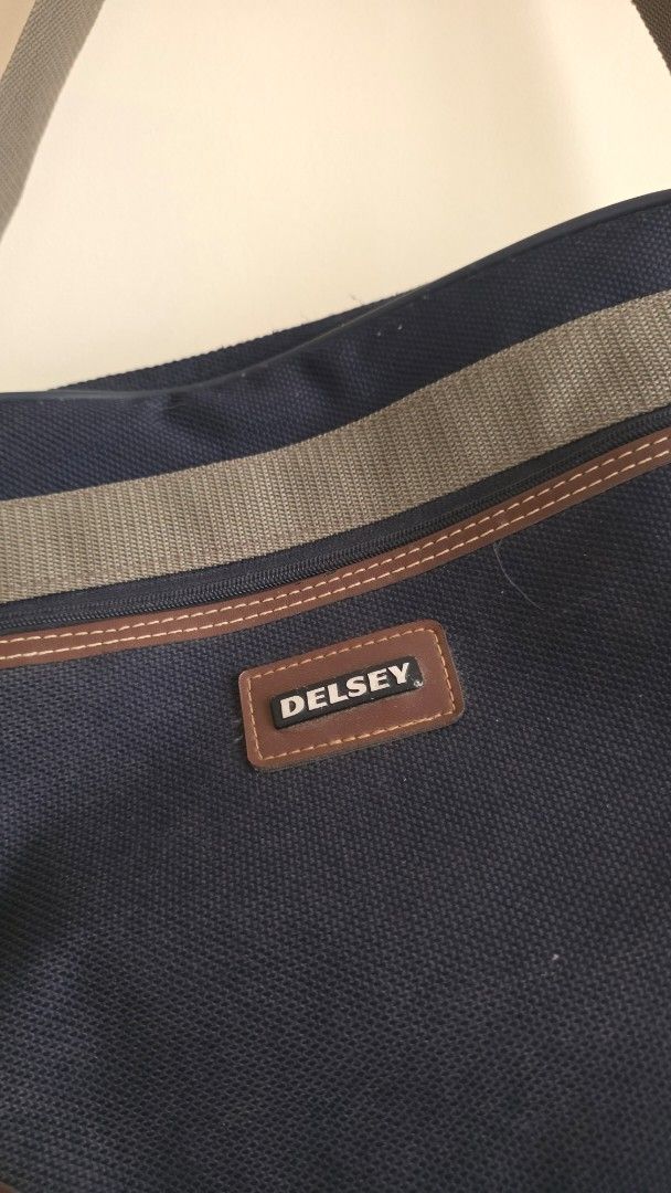 Delsey Canvas Messenger Bag with Shoulder Strap (Category: Sling Bags) located in Las Pinas. Submitted by lovedbymariee (Listing ID 1470187160, Image 3). Description: - Brand: Delsey - Color: Dark navy blue canvas with brown leather trim - Design: Front zippered pocket with olive green stripe and included padlock - Comfort: Adjustable canvas shoulder strap with padded grip handle.