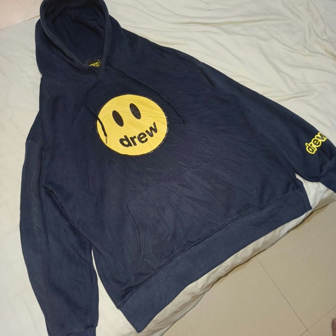 Drew House Mascot Hoodie Navy Blue (Category: Coats, Jackets and Outerwear) located in Manila. Submitted by collinvien123 (Listing ID 1470281237, Image 3). Description: - Brand: Drew House - Color: Dark Navy Blue with Yellow Graphics - Size: Large - Design: Large smiley face with 'drew' on chest, yellow lettering on left sleeve - Material: Comfortable fleece cotton - Features: Adjustable drawstrings with metal tips, front kangaroo pocket, ribbed 