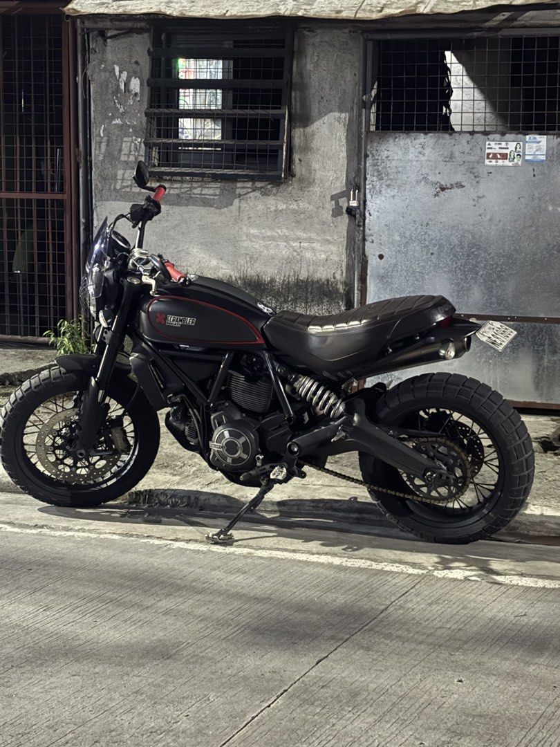 Ducati Scrambler Matte Black Motorcycle (Category: Motorbikes for Sale) located in Caloocan City. Submitted by iampodave0620 (Listing ID 1470178977, Image 3). Description: Matte black finish with red accents on the tank and handlebars. Dual-sport tires with wire-spoke wheels, ribbed brown leather seat, upright handlebars with bar-end mirrors, front windscreen. Loud exhaust setup installed. Street legal, clean papers ready for transfer..