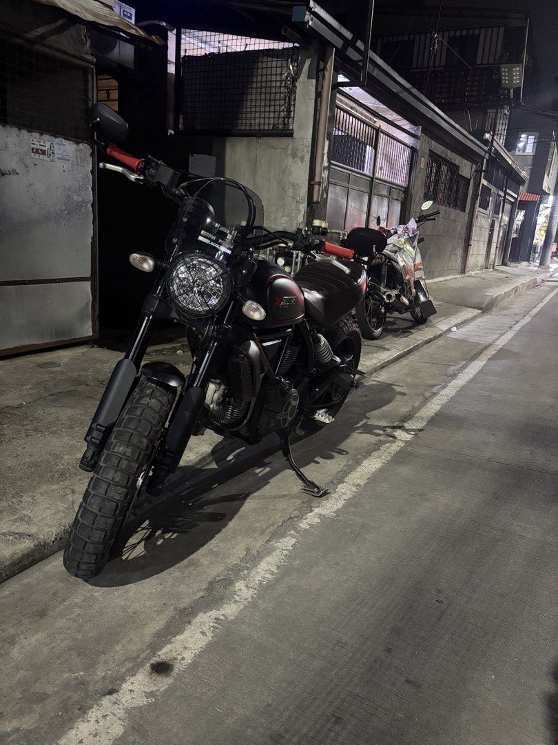 Ducati Scrambler Matte Black Motorcycle (Category: Motorbikes for Sale) located in Caloocan City. Submitted by iampodave0620 (Listing ID 1470178977, Image 2). Description: Matte black finish with red accents on the tank and handlebars. Dual-sport tires with wire-spoke wheels, ribbed brown leather seat, upright handlebars with bar-end mirrors, front windscreen. Loud exhaust setup installed. Street legal, clean papers ready for transfer..
