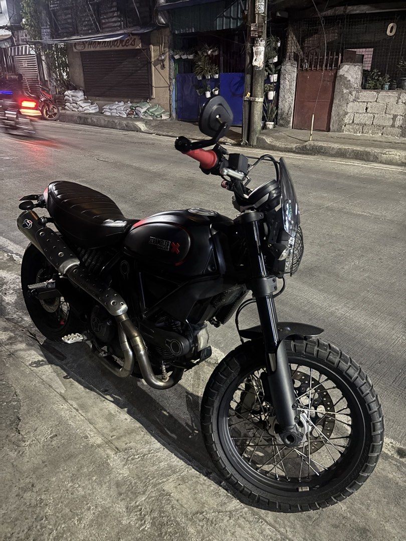 Ducati Scrambler Matte Black Motorcycle (Category: Motorbikes for Sale) located in Caloocan City. Submitted by iampodave0620 (Listing ID 1470178977, Image 1). Description: Matte black finish with red accents on the tank and handlebars. Dual-sport tires with wire-spoke wheels, ribbed brown leather seat, upright handlebars with bar-end mirrors, front windscreen. Loud exhaust setup installed. Street legal, clean papers ready for transfer..