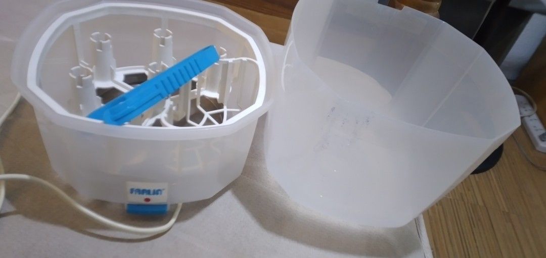 Farlin electric bottle sterilizer and dryer (Category: Breastfeeding & Bottle Feeding) located in Quezon City. Submitted by roxasjr86 (Listing ID 1470195711, Image 3). Description: - Brand: Farlin - Type: Electric bottle sterilizer - Color: Translucent white with blue tongs included - Features: Removable cover, internal bottle rack, and multiple prongs to hold bottles upright - Controls: Easy-access power switch button on the front with attached 