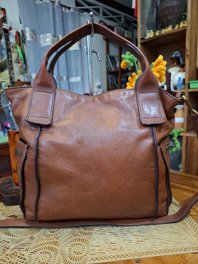 Fossil Brown Leather Shoulder Bag Handbag (Category: Shoulder Bags) located in Libon. Submitted by jaladzarmi80045 (Listing ID 1470237034, Image 3). Description: - Brand: Fossil - Material: Genuine pebbled leather in rich brown with dark brown trim - Hardware: Gold-tone with front logo plaque - Straps: Double top handles and an adjustable/detachable shoulder strap - Closure & Pockets: Zip top closure with an exterior side zip pocket.