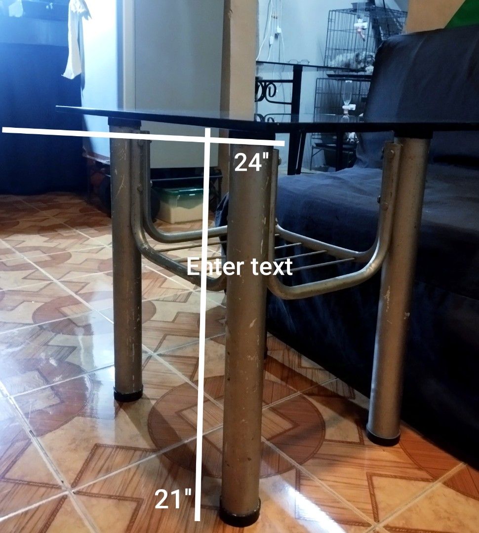 Glass Top Metal Frame Coffee Table With Lower Shelf (Category: Tables & Sets) located in Mandaluyong City. Submitted by perfectfashion.mnl (Listing ID 1470288966, Image 1). Description: - Glass top coffee table with a sturdy metal tubular frame - Dimensions: 24 inches x 21 inches - Features a lower wire shelf for extra storage - Perfect for living rooms, bedrooms, or small apartments - Condition: Silver painted legs show paint chipping and wear a