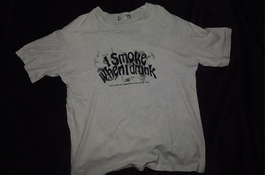 Graphic T-Shirt I Smoke When I Drunk (Category: Tshirts & Polo Shirts ) located in Caloocan City. Submitted by yat0zu (Listing ID 1470279084, Image 1). Description: - Color:WHITE/GRAY-ISH - Style: Oversized / Relaxed fit - Graphic: Front print with bold black text 'I Smoke When I Drunk' - Material: Soft, breathable - Details: Classic crew neckline, short sleeves - Condition: PRE—LOVED.