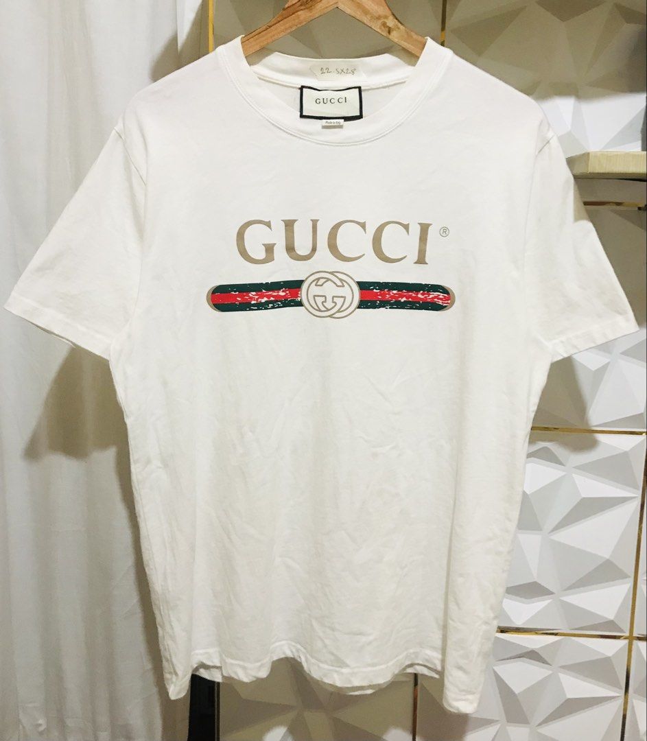Gucci Vintage Logo Tee White (Category: Luxury Apparel) located in Manila. Submitted by luxurybrandedthrift05 (Listing ID 1470215312, Image 1). Description: - Authentic Gucci cotton t-shirt in white - Features distressed logo graphic across the chest - Classic red and green web stripe with interlocking GG logo - Made in Italy tag at the collar - Measurements: 22.5 inches (pit to pit) by 28 inches (length) - Short sleeves with ribbed crewneck - Cl