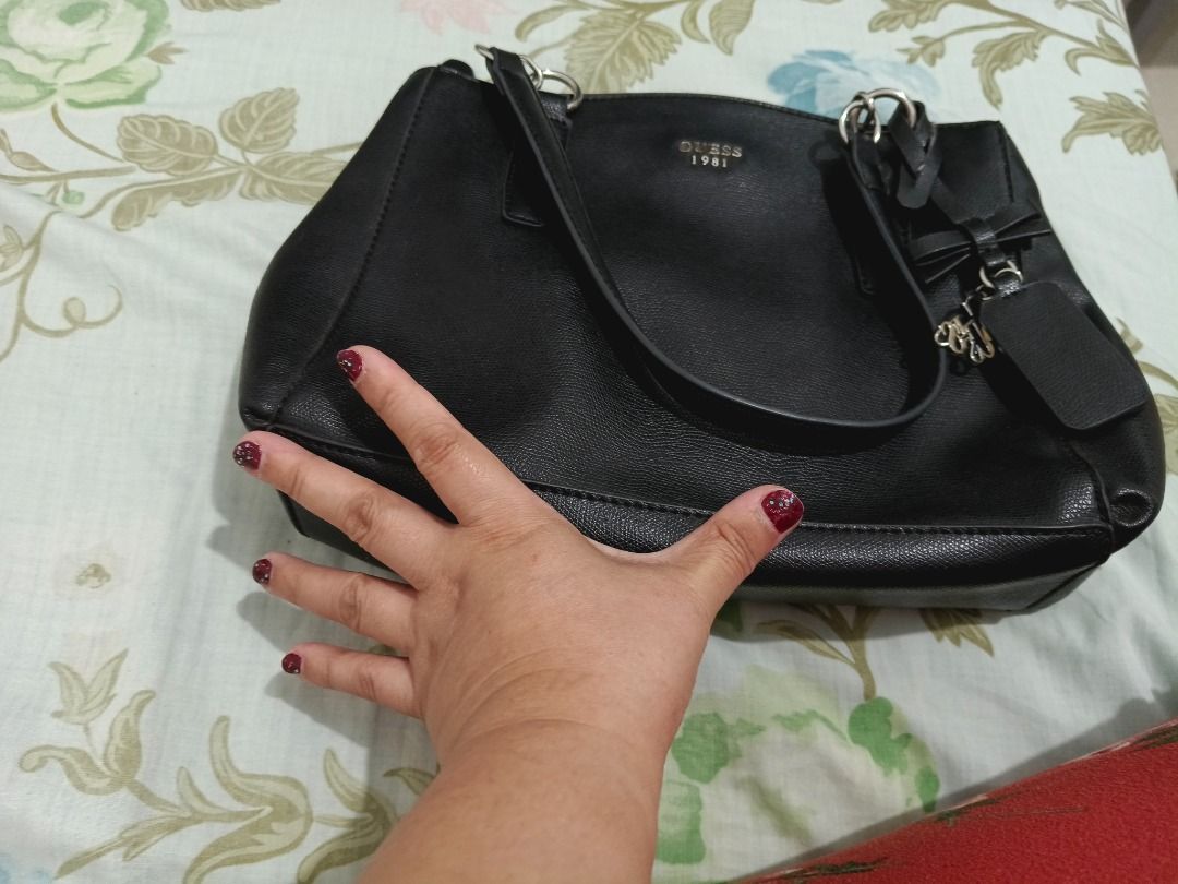 Guess 1981 Black Tote Bag with Bow Charm (Category: Tote Bags) located in Las Pinas. Submitted by tepffwayne6901 (Listing ID 1470168316, Image 3). Description: Original Guess Bag 2 compartment Good as new - Brand: Guess (1981 collection) - Color: Classic Black - Material: Textured faux leather with printed fabric lining - Straps: Dual shoulder straps - Accents: Hanging bow charm and metal front logo lettering - Closure & Storage: Magnetic snap cl