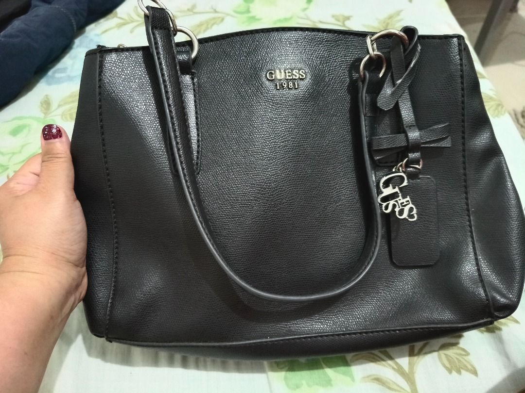 Guess 1981 Black Tote Bag with Bow Charm (Category: Tote Bags) located in Las Pinas. Submitted by tepffwayne6901 (Listing ID 1470168316, Image 1). Description: Original Guess Bag 2 compartment Good as new - Brand: Guess (1981 collection) - Color: Classic Black - Material: Textured faux leather with printed fabric lining - Straps: Dual shoulder straps - Accents: Hanging bow charm and metal front logo lettering - Closure & Storage: Magnetic snap cl