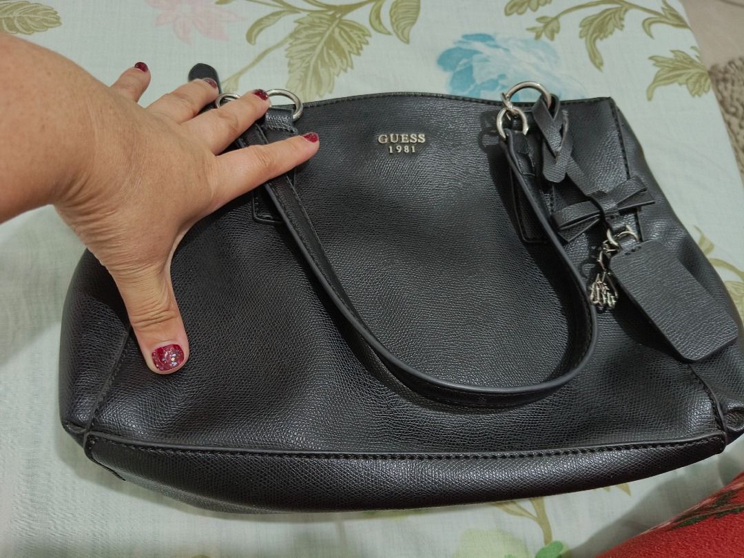 Guess 1981 Black Tote Bag with Bow Charm (Category: Tote Bags) located in Las Pinas. Submitted by tepffwayne6901 (Listing ID 1470168316, Image 2). Description: Original Guess Bag 2 compartment Good as new - Brand: Guess (1981 collection) - Color: Classic Black - Material: Textured faux leather with printed fabric lining - Straps: Dual shoulder straps - Accents: Hanging bow charm and metal front logo lettering - Closure & Storage: Magnetic snap cl