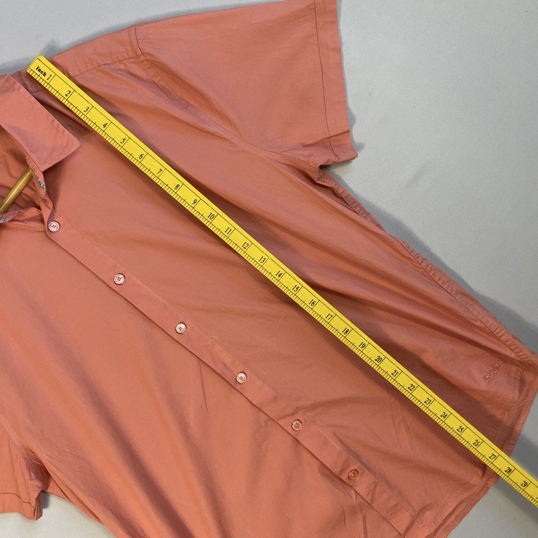 GUESS | Peach Solid Short-Sleeve Button-Down Shirt Size L (Category: Tshirts & Polo Shirts ) located in Norzagaray. Submitted by sevenjscloset (Listing ID 1470273898, Image 3). Description: - Brand: GUESS - Style: Short-sleeve button-down with classic collar - Color: Solid peach - Size: Large on tag - Measurements: 27.5" length x 20.5" width - Fit Reference: Modeled by 5'10" and 70kg individual - Condition: Excellent, no issues or flaws spotted.