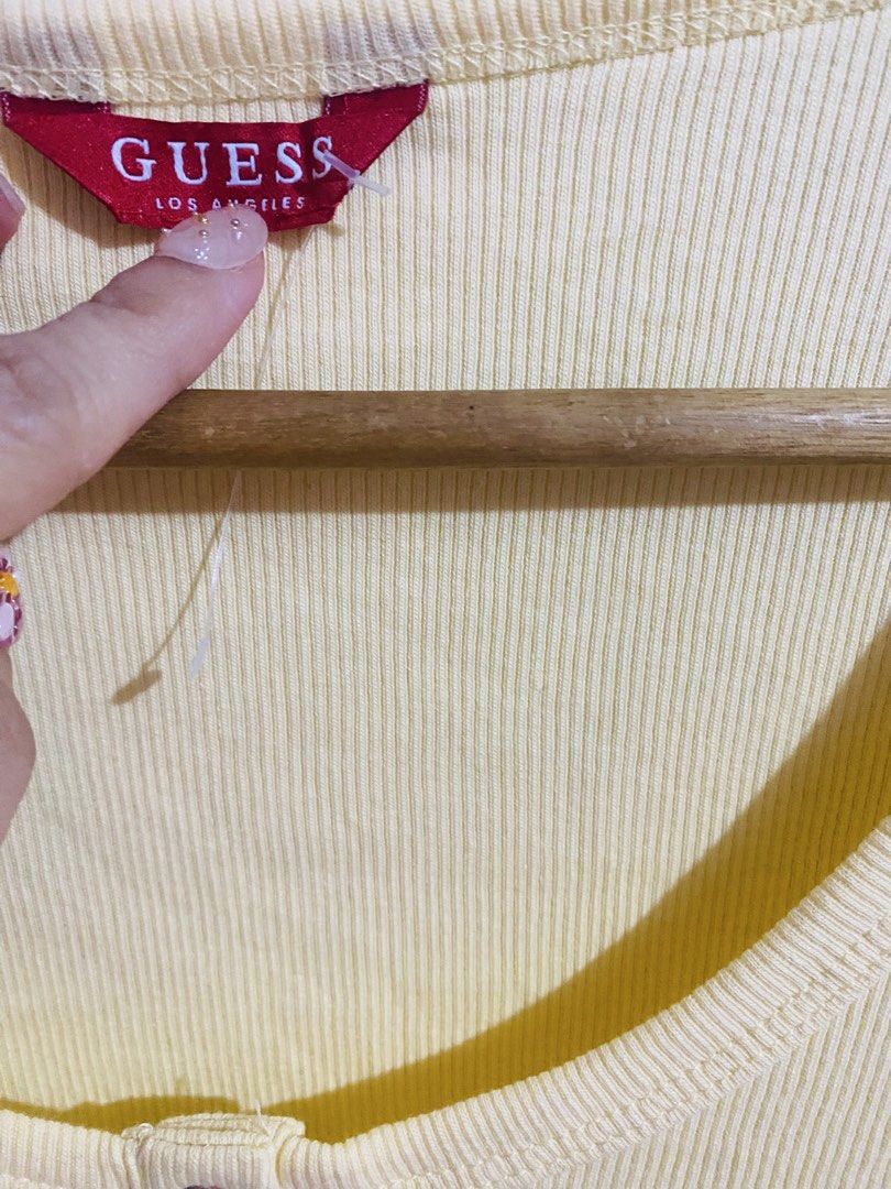 Guess Yellow Ribbed Button Henley Top (Category: Blouses) located in Cavite. Submitted by luxxe.muse (Listing ID 1470289015, Image 3). Description: - Brand: Guess - Color: Trendy pastel butter yellow - Style: Slim fit basic top with scoop neck and short sleeves - Details: 3 decorative front buttons and signature metal Guess logo tag near the hem - Material: Soft, stretchy ribbed cotton for all-day comfort - Condition: Excellent / Like new - Perfe