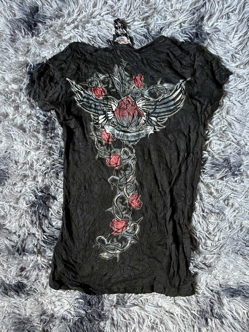 Harley-Davidson Black Rose & Wing Top (Category: Tshirts & Polo Shirts ) located in Tarlac. Submitted by rhandell_collectives (Listing ID 1470194214, Image 2). Description: - Brand: Harley-Davidson - Size: Medium - Color/Fabric: Black with crinkled texture (54% cotton blend) - Neckline: V-neck with two buttons - Sleeves: Short sleeves - Front Design: Red roses and thorny vines graphic on the left side - Back Design: Large signature winged banner 