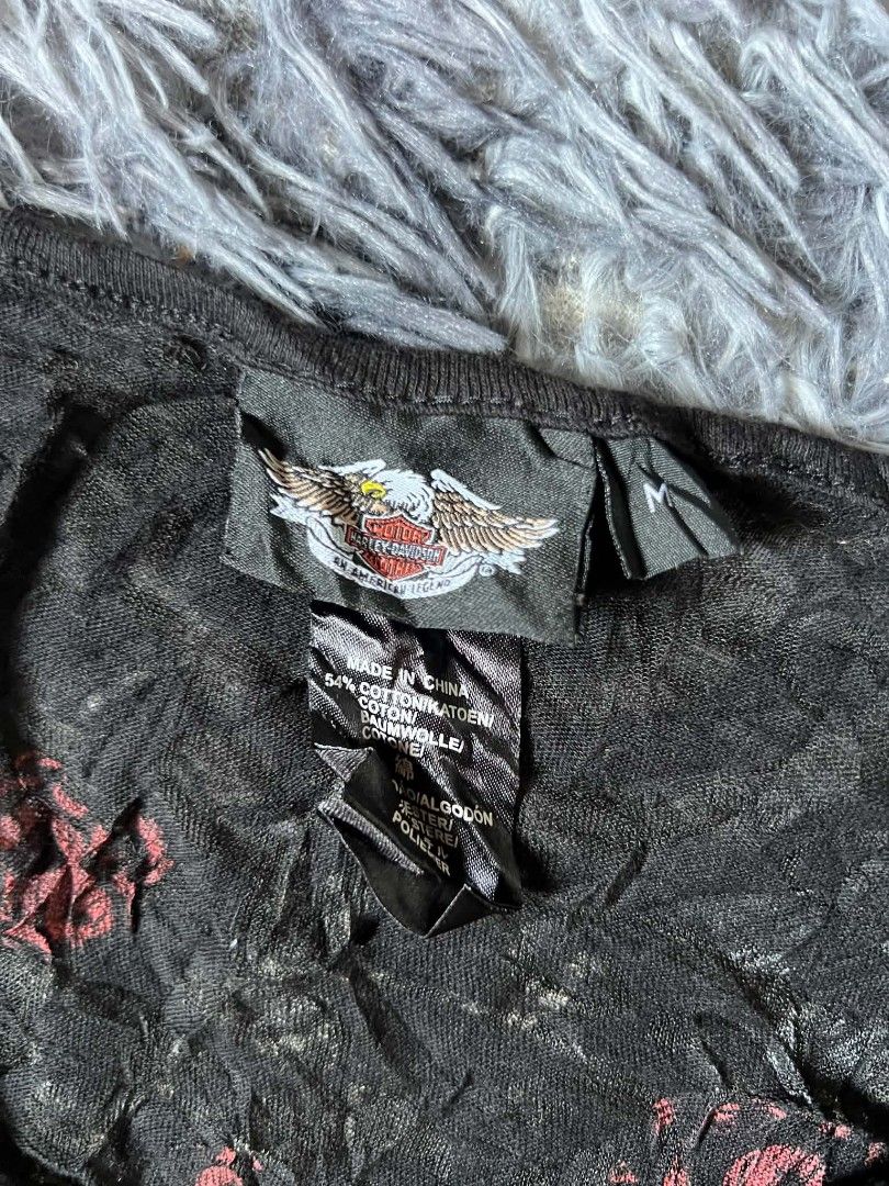 Harley-Davidson Black Rose & Wing Top (Category: Tshirts & Polo Shirts ) located in Tarlac. Submitted by rhandell_collectives (Listing ID 1470194214, Image 3). Description: - Brand: Harley-Davidson - Size: Medium - Color/Fabric: Black with crinkled texture (54% cotton blend) - Neckline: V-neck with two buttons - Sleeves: Short sleeves - Front Design: Red roses and thorny vines graphic on the left side - Back Design: Large signature winged banner 