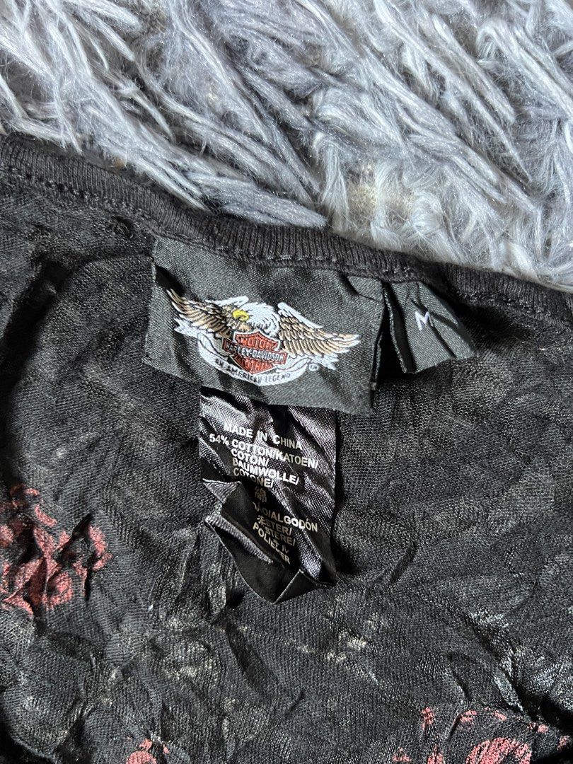 Harley-Davidson Black Rose Wing Graphic Top (Category: Shirts) located in Tarlac. Submitted by zealbird-9188e4 (Listing ID 1470281069, Image 2). Description: - Brand: Harley-Davidson - Style: V-neck top with short cap sleeves, button placket, and crinkle-texture fabric - Size: M - Material: 54% cotton blend - Front Design: Large rose and barbed wire graphic on the left side - Back Design: Massive winged rose graphic with Harley-Davidson banner - 