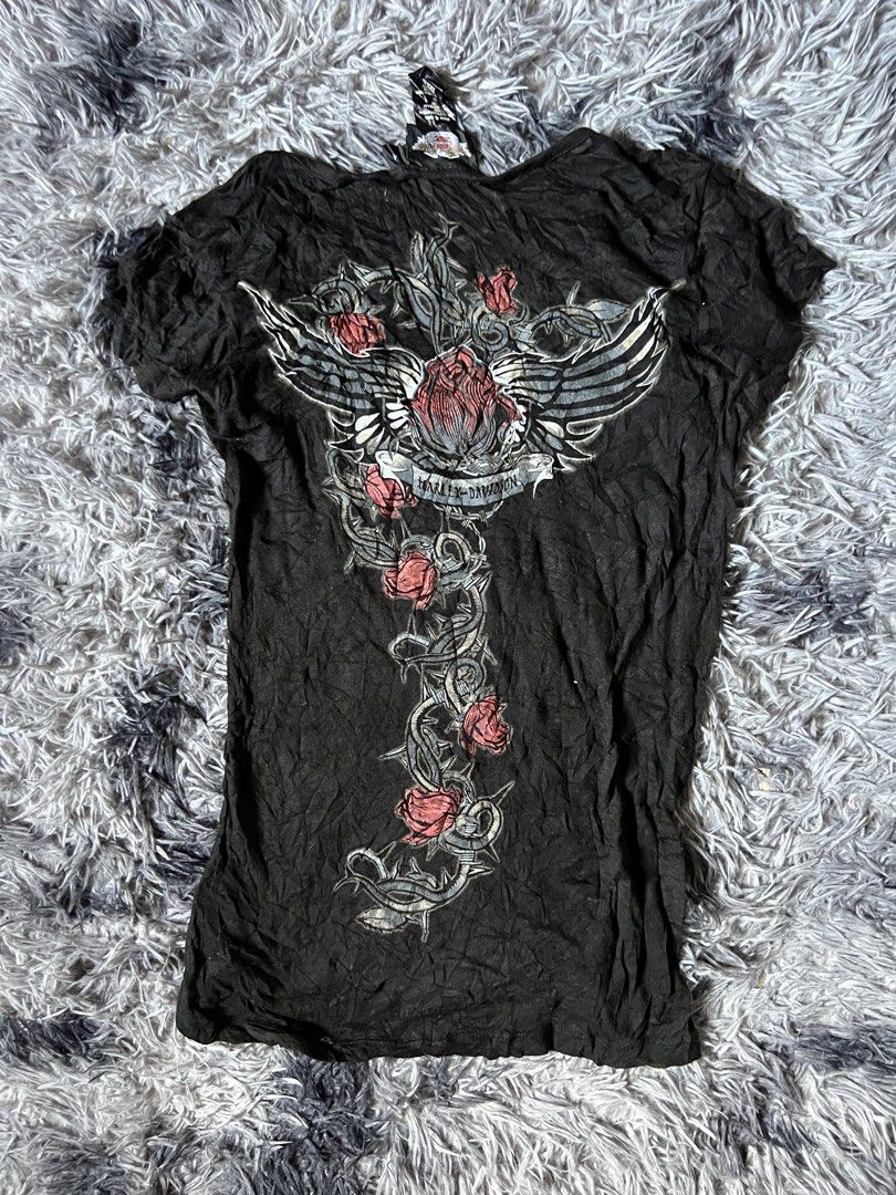 Harley-Davidson Black Rose Wing Graphic Top (Category: Shirts) located in Tarlac. Submitted by zealbird-9188e4 (Listing ID 1470281069, Image 3). Description: - Brand: Harley-Davidson - Style: V-neck top with short cap sleeves, button placket, and crinkle-texture fabric - Size: M - Material: 54% cotton blend - Front Design: Large rose and barbed wire graphic on the left side - Back Design: Massive winged rose graphic with Harley-Davidson banner - 