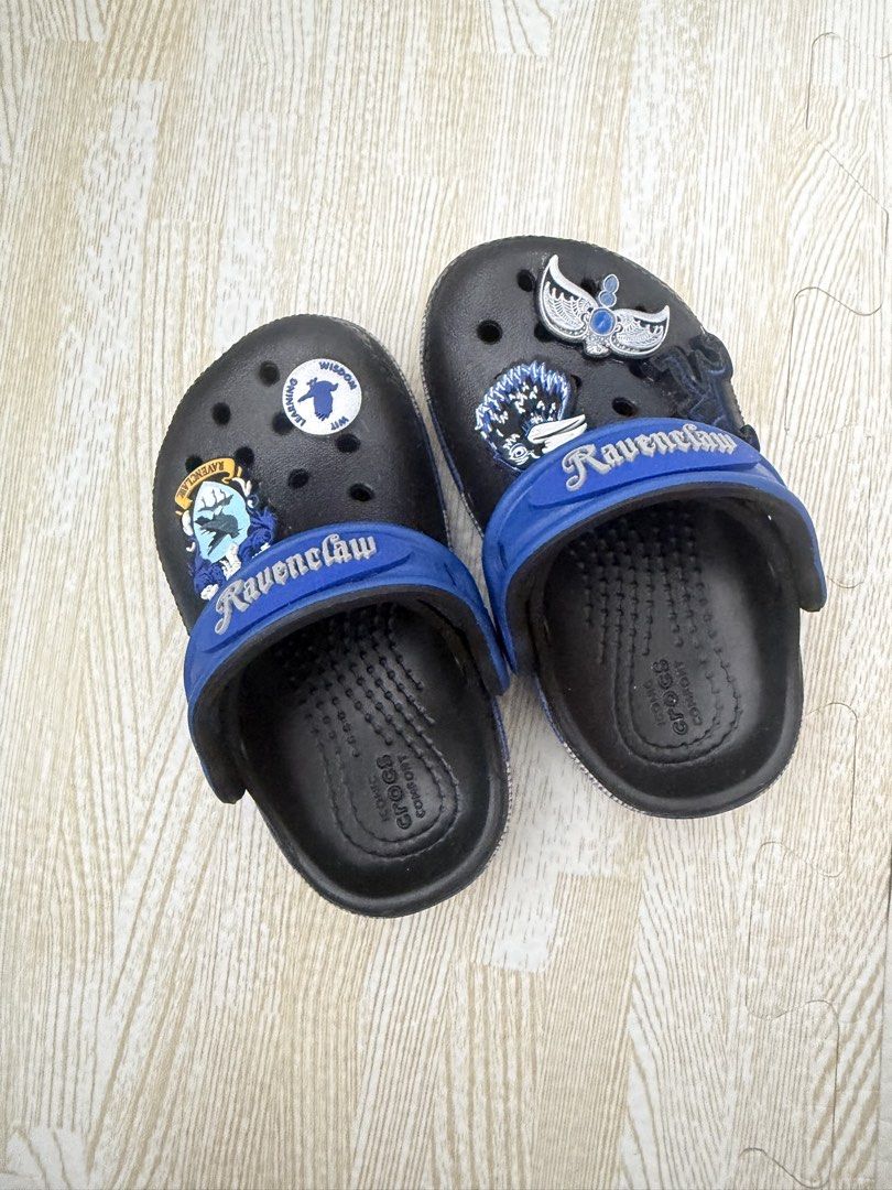 Harry Potter Ravenclaw Crocs Clogs Size C6 (Category: Babies & Kids Fashion) located in Naga. Submitted by suit_yourslf (Listing ID 1470151376, Image 2). Description: - Item: Harry Potter Ravenclaw Crocs Clog Sandals - Size: C6 (indicated on outsole) - Color/Design: Black base with blue heel strap and Ravenclaw lettering - Included Charms: Ravenclaw crest, raven, and house motto badge - Features: Slip-on design and ventilation holes - Condition: 