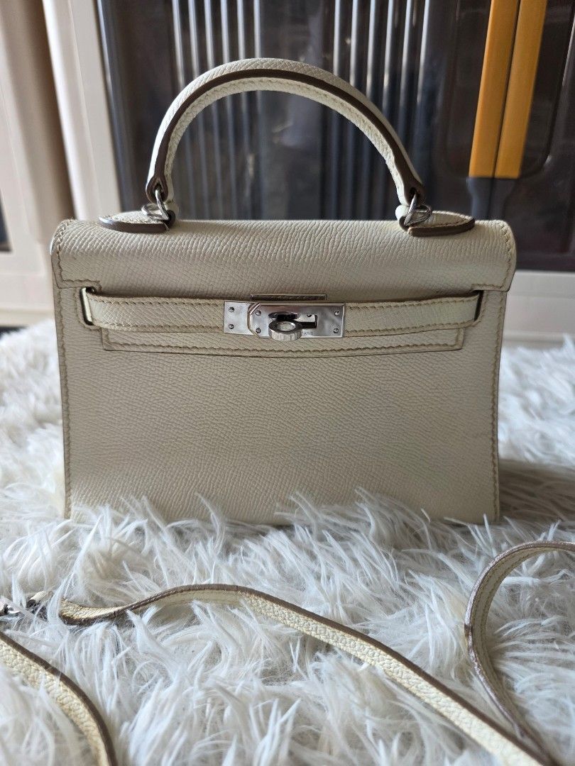 Hermes Paris White Leather Mini Kelly Handbag (Category: Cross-body Bags) located in Lemery. Submitted by venus23 (Listing ID 1470145469, Image 1). Description: - Hermes Paris Mini Kelly handbag - White textured leather with sleek silver-tone hardware and signature clasp closure - Features a sturdy single top handle and a convenient detachable matching shoulder strap - Compact structure (approx. 7 inches across) with protective metal feet on the 