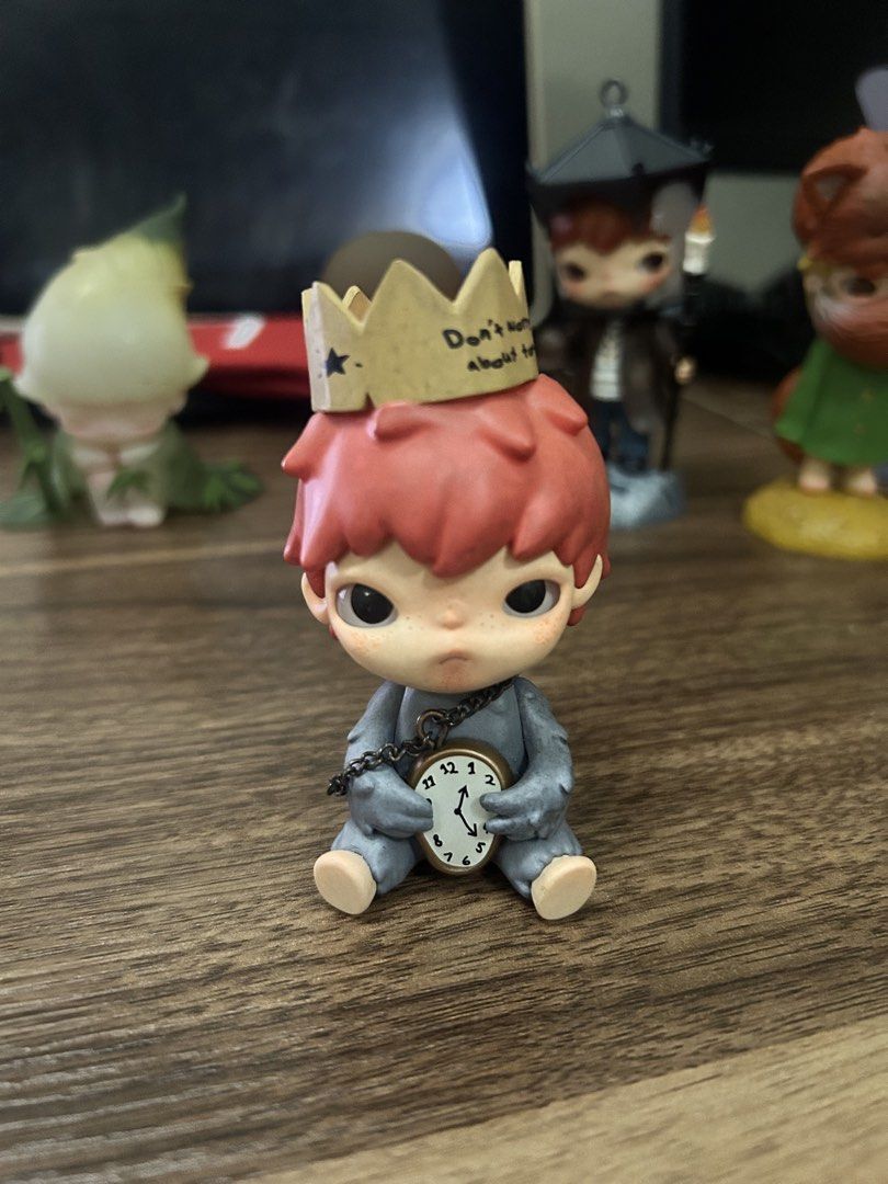 Hirono Shelter (Category: Designer & Blind Box Toys) located in Manila. Submitted by mihos.garage.sale (Listing ID 1470186726, Image 1). Description: - Features striking red hair, a grey outfit, and cute big eyes - Wears a golden crown inscribed with 'Don't worry about tomorrow' and 'Matthew 6:34' - Comes with a mini clock on a metal chain accessory - Collected and displayed carefully on a shelf, smoke-free home.