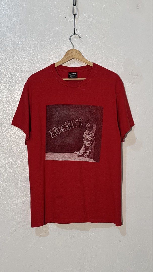 Hockey Skateboards Red Graphic Tee Medium (Category: Tshirts & Polo Shirts ) located in Manila. Submitted by glano (Listing ID 1470298137, Image 1). Description: - Brand: Hockey Skateboards - Color: Red - Size: Medium (Tagged) - Material: 100% Cotton - Design: Bold front graphic of a person in a straightjacket with stylized brand text - Details: Crew neckline, standard short sleeves - Condition: Clean fabric with minimal wear on tags and graphic.