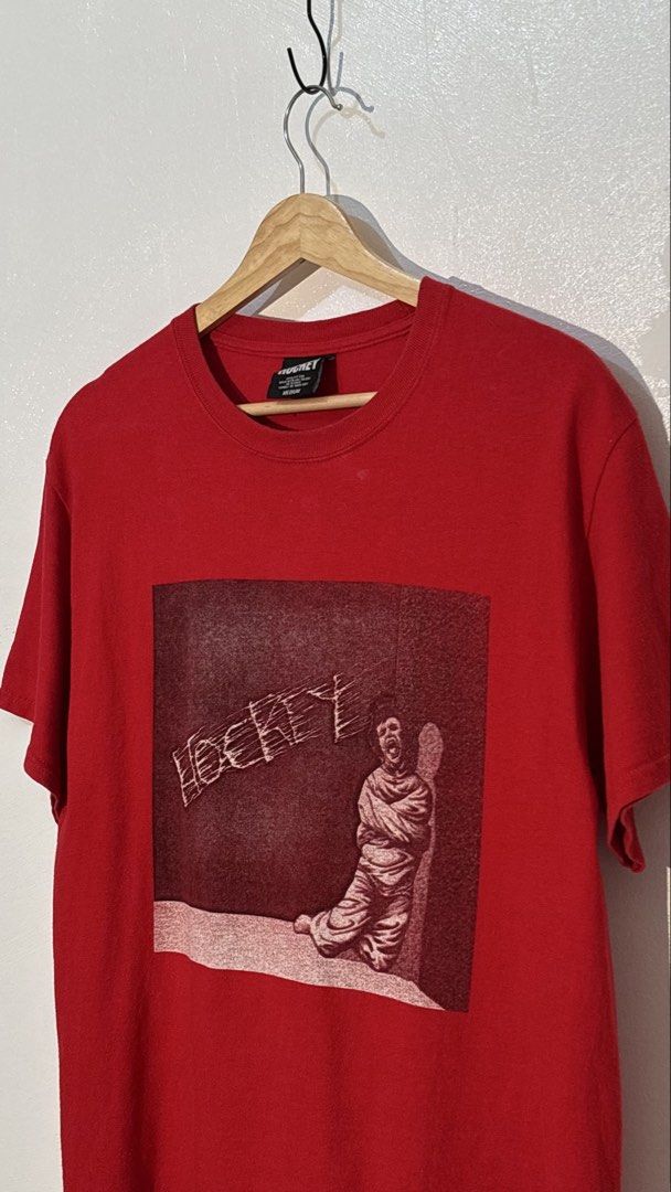 Hockey Skateboards Red Graphic Tee Medium (Category: Tshirts & Polo Shirts ) located in Manila. Submitted by glano (Listing ID 1470298137, Image 2). Description: - Brand: Hockey Skateboards - Color: Red - Size: Medium (Tagged) - Material: 100% Cotton - Design: Bold front graphic of a person in a straightjacket with stylized brand text - Details: Crew neckline, standard short sleeves - Condition: Clean fabric with minimal wear on tags and graphic.