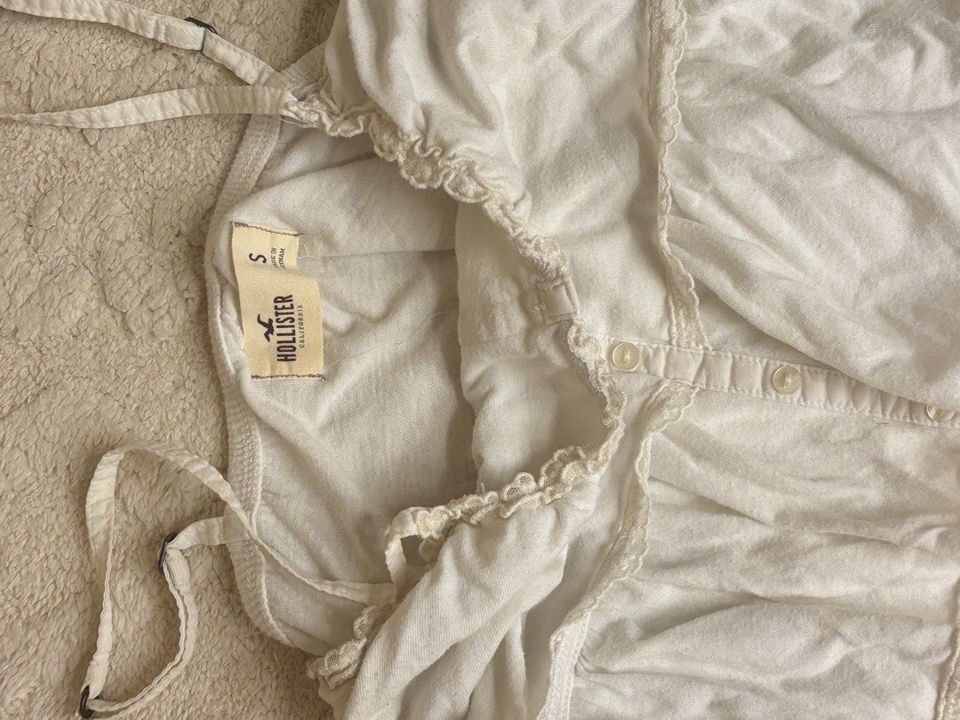 Hollister White Tiered Button-Front Cami Top (Category: Sleeveless) located in Quezon City. Submitted by lovedbysloane (Listing ID 1470248450, Image 2). Description: - Brand: Hollister - Size: Small - Color: White - Design: Tiered and layered with delicate lace trim - Closure: Center button-front with small white buttons - Straps: Adjustable spaghetti straps - Material: Lightweight, soft cotton fabric - Condition: Excellent.