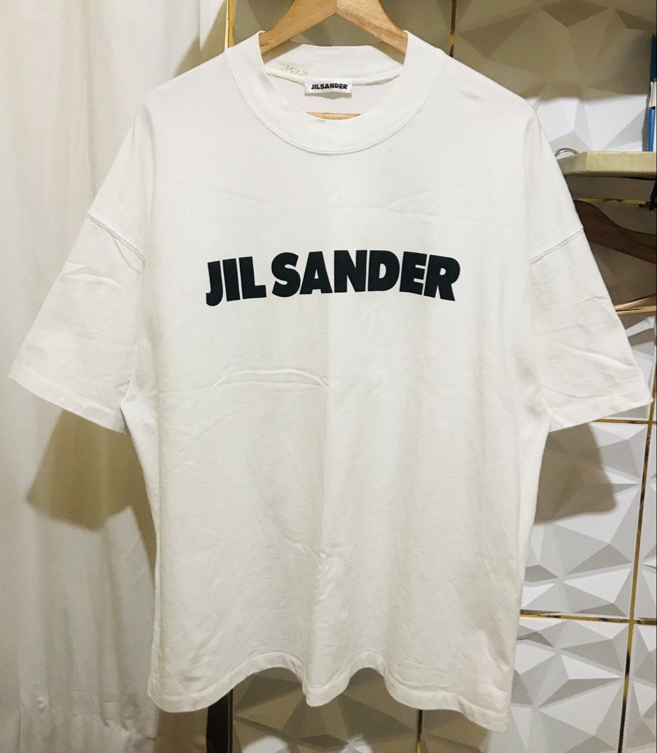 Jil Sander White Logo Tee (Category: Luxury Apparel) located in Manila. Submitted by luxurybrandedthrift05 (Listing ID 1470214106, Image 1). Description: - Brand: Jil Sander - Color: White with large black front logo - Material: 100% heavy cotton, made in Italy - Design: Short sleeves, crew neck collar - Condition: Clean fabric, excellent quality - Authenticity: Includes full interior care and product code labels.