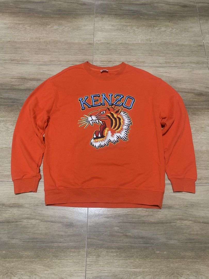 Kenzo Orange Tiger Embroidered Sweatshirt Size M (Category: Luxury Apparel) located in Tarlac. Submitted by luxurious_apparel (Listing ID 1470264373, Image 1). Description: - Brand: Kenzo - Color: Vibrant Orange - Size: Medium (Made in Portugal) - Design: Bold embroidered tiger head graphic with blue lettering - Details: Classic crew neck with ribbed collar, cuffs, and hem - Condition: Clean interior and well-maintained.