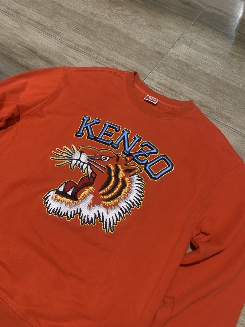 Kenzo Orange Tiger Embroidered Sweatshirt Size M (Category: Luxury Apparel) located in Tarlac. Submitted by luxurious_apparel (Listing ID 1470264373, Image 2). Description: - Brand: Kenzo - Color: Vibrant Orange - Size: Medium (Made in Portugal) - Design: Bold embroidered tiger head graphic with blue lettering - Details: Classic crew neck with ribbed collar, cuffs, and hem - Condition: Clean interior and well-maintained.