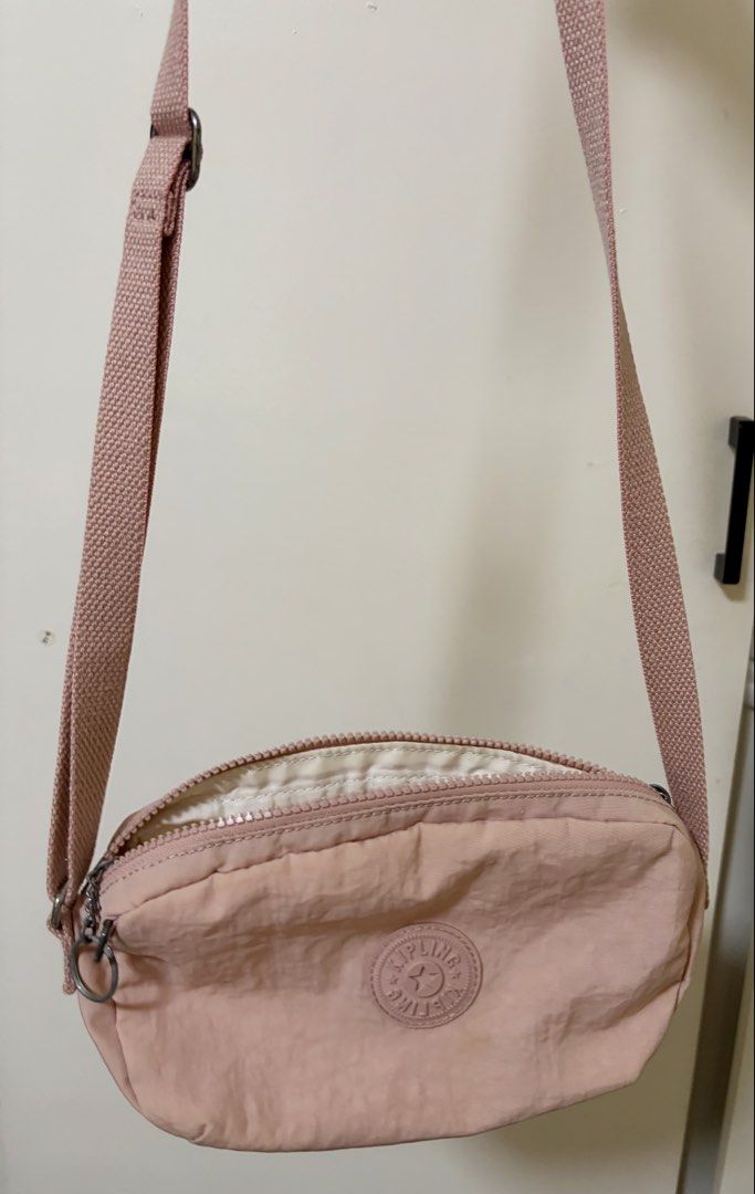 Kipling Pink Nylon Crossbody Bag (Category: Cross-body Bags) located in Angeles City. Submitted by chaegyoung (Listing ID 1470240779, Image 1). Description: - Authentic Kipling crossbody bag in a charming light pink shade - Durable nylon material with an adjustable shoulder strap for comfort - Secure zipper top closure opening to a spacious lined interior - Signature round Kipling logo patch on the front - Flaw note: Some dirt marks and stains ar