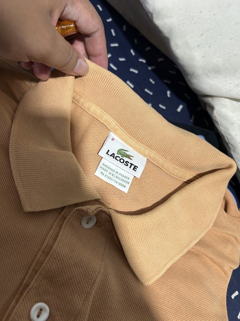 Lacoste Orange Polo Shirt Size 8 (Category: Tshirts & Polo Shirts ) located in San Simon. Submitted by ericdeinla69664 (Listing ID 1470189098, Image 2). Description: - Brand: Lacoste - Color: Vibrant Orange - Size: 8 - Material: 100% Cotton - Design: Classic two-button collar with embroidered green crocodile logo - Origin: Designed in France, Made in El Salvador - Style: Solid color casual wear - Authenticity tags attached (RN 87651, CA 16998).