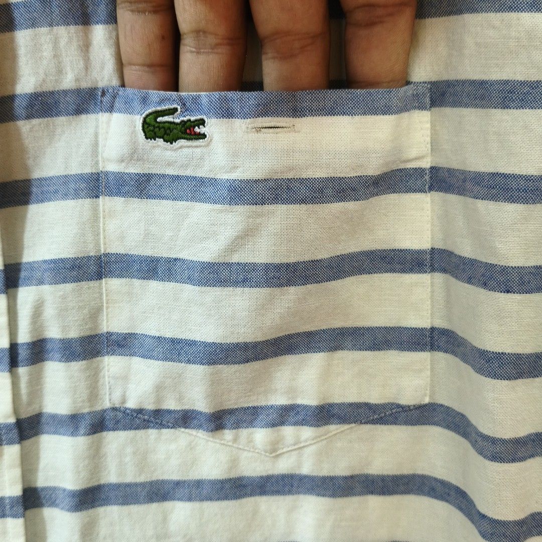 Lacoste Striped Short Sleeve Linen Blend Button-Down Shirt (Category: Tshirts & Polo Shirts ) located in Quezon City. Submitted by inrelationthrift (Listing ID 1470194020, Image 3). Description: - Brand: Lacoste - Style: Short-sleeve button-down shirt with chest pocket - Design: White base with blue horizontal stripes on the upper body and red stripes near the hem - Logo: Iconic embroidered green crocodile on the chest - Material: 80% Cotton, 20%