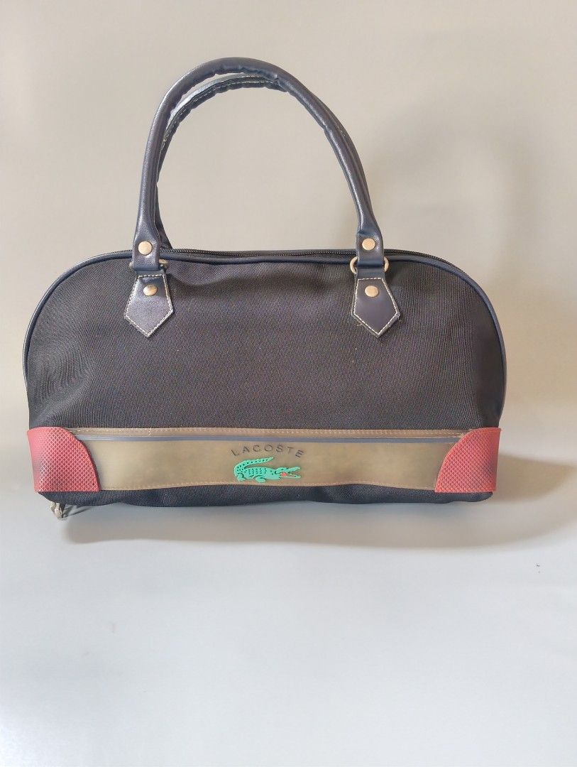 Lacoste Vintage Bag (Category: Luxury Bags & Wallets) located in Cagayan de Oro. Submitted by warmbird-f84aab (Listing ID 1470174947, Image 2). Description: - Black canvas body + red accent details - Double top handles, zip closure - 2 Lacoste engraved zipper pulls - Interior brand tag intact - Condition: Pre-loved, good overall. Minor fading on front leather band — natural patina, no tears/rips. Zippers work perfectly..