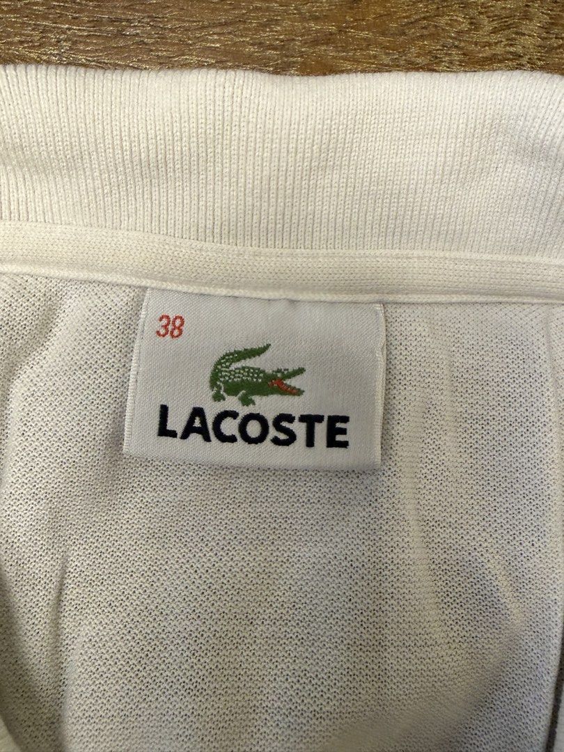 Lacoste White Polo Shirt Size 38 (Category: Shirts) located in Muntinlupa City. Submitted by el1b12345 (Listing ID 1470186067, Image 3). Description: - White Lacoste polo shirt in women's - size 38. - L - 22" - W - 17" - Striped collar and sleeve cuffs in brown, black, and gold tones. - Classic fit with four-button placket and embroidered crocodile logo on the chest. - Cotton petit pique fabric. - Clean condition, no major flaws found. - mop: Gca