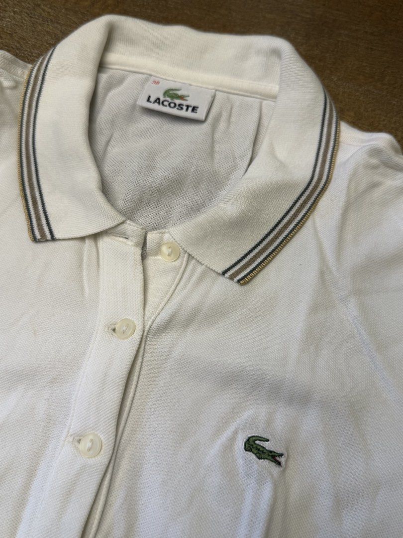 Lacoste White Polo Shirt Size 38 (Category: Shirts) located in Muntinlupa City. Submitted by el1b12345 (Listing ID 1470186067, Image 2). Description: - White Lacoste polo shirt in women's - size 38. - L - 22" - W - 17" - Striped collar and sleeve cuffs in brown, black, and gold tones. - Classic fit with four-button placket and embroidered crocodile logo on the chest. - Cotton petit pique fabric. - Clean condition, no major flaws found. - mop: Gca