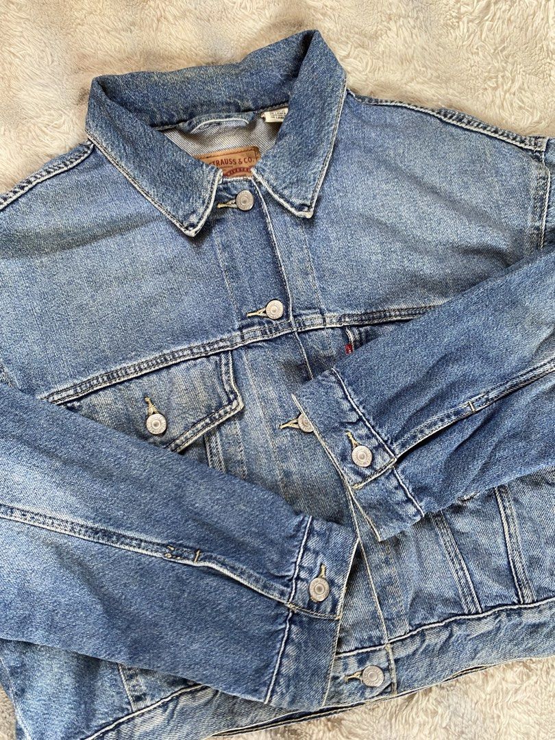 Levi's Vintage Fit Trucker Denim Jacket (Category: Coats, Jackets and Outerwear) located in Andop. Submitted by safewater-895a (Listing ID 1470279741, Image 3). Description: - Brand: Levi's - Style: Classic denim jacket with cropped fit - Color: Medium wash blue - Size: Medium - Features: Metal embossed buttons, iconic red tab on chest pocket, two buttoned chest pockets, and side pockets - Condition: Sturdy denim with regular wear - Dimes: 23x20.
