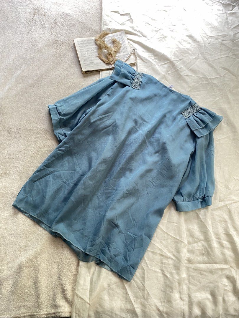 Light blue ruffle blouse with pearl trim Medium 37 (Category: Blouses) located in Poro. Submitted by joyceyuu (Listing ID 1470169049, Image 3). Description: - Color: Light blue with a subtle sheen - Style: Loose fit, perfect for casual or dressed-up looks - Neckline: Square neck with elegant pearl and lace detailing - Details: Eye-catching ruffles across the front shoulders - Sleeves: Short puff sleeves with comfortable gathered cuffs - Material: